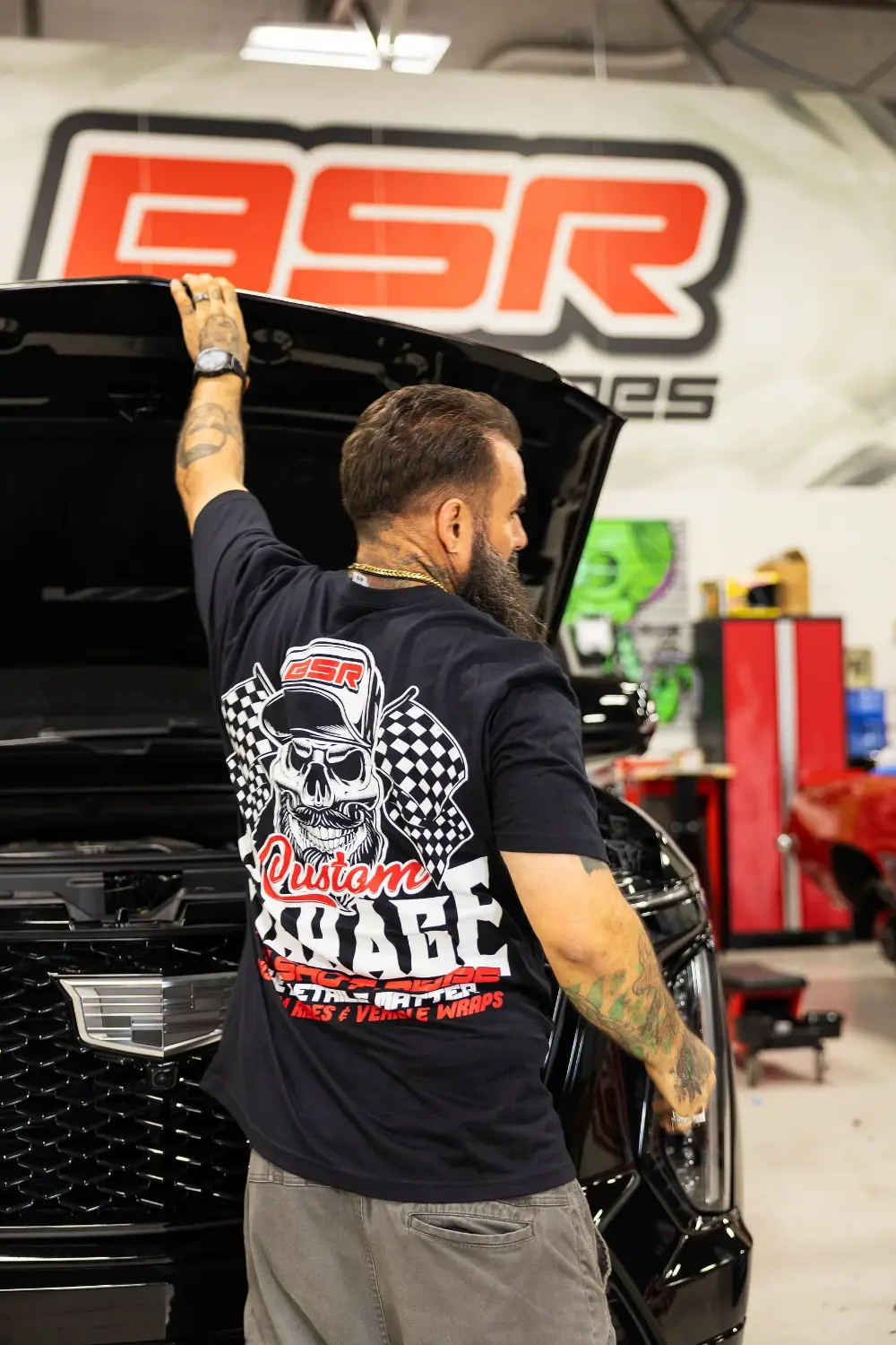 Chris Joerger under the hood of a Cadillac Escalade-V in front of the Big Shot Rides logo wall