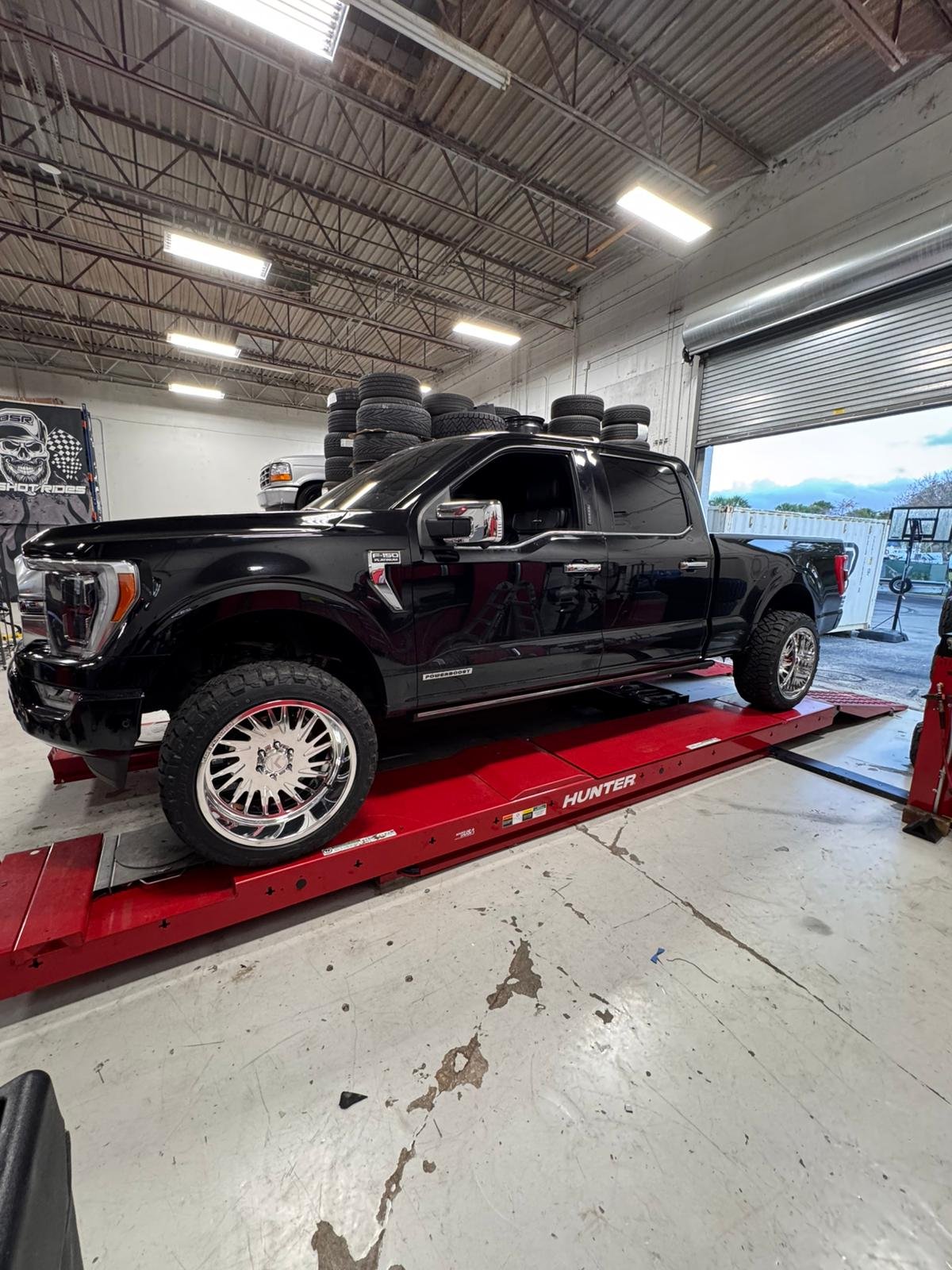 Black Ford F-450 dually on the Hunter rack at Big Shot Rides with stacks of new tires in Coconut Creek FL
