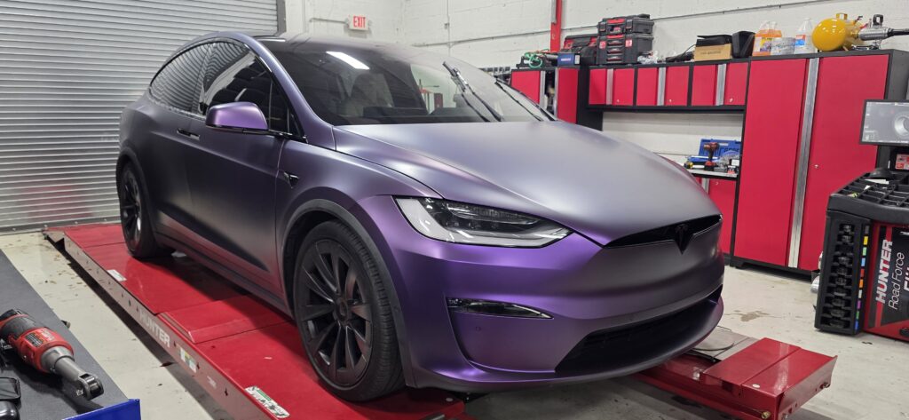 Tesla Model X in a satin purple color-shift wrap on the alignment rack at Big Shot Rides in Coconut Creek, Florida